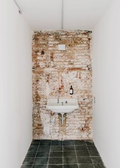 a white sink sitting in the corner of a room next to a brick wall and tiled floor