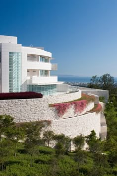 a white building with flowers growing on it's side and the ocean in the background