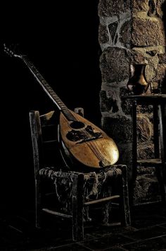 a guitar sitting on top of a wooden chair next to a stone wall in a dark room