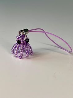 a purple and black beaded key chain on a white surface with a cord attached to it