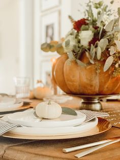 a wooden table topped with white plates and silverware next to a vase filled with flowers