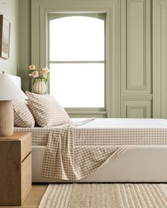 a bed sitting in front of a window next to a wooden night stand with flowers on it