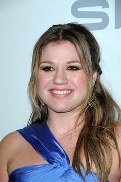 a woman in a blue dress smiling at the camera with her hair pulled back and wearing large earrings