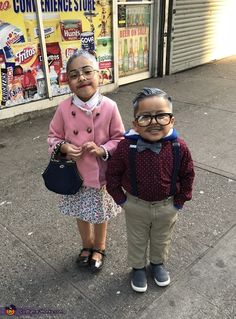 two young children standing next to each other in front of storefronts and signs