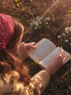 a woman is sitting in the grass reading a book and writing something on her notebook