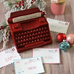 an old fashioned red typewriter sitting on top of a wooden floor next to christmas decorations