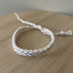 two white bracelets sitting on top of a wooden table next to a string with a tassel hanging from it