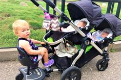 two babies sit in strollers next to each other on the sidewalk near a fence