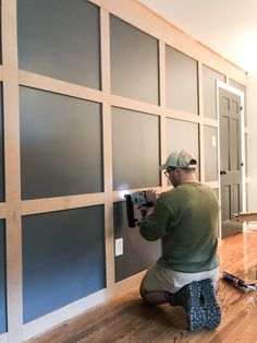 a man that is kneeling down on the floor with a drill in his hand and some paint