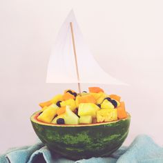 a boat made out of watermelon is sitting on top of a bowl filled with fruit