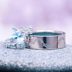 two wedding rings sitting on top of a rock with blue stones in the middle and one ring surrounded by leaves