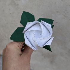 someone is holding an origami flower with sheet music notes on it and green leaves