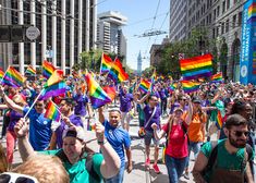 a large group of people walking down the street holding rainbow flags and waving their hands