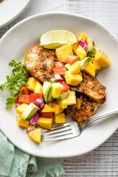 a white plate topped with chicken, mango salsa and avocado wedges next to a fork