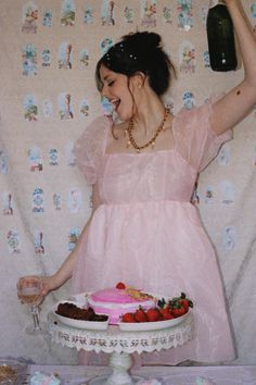 a woman standing in front of a table with a cake and wine bottle on it