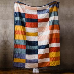 a person standing in front of a wall with a large colorful blanket hanging from it's side