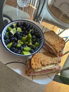 a sandwich cut in half next to a bowl of blueberries and kiwis