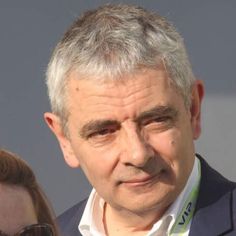 an older man with grey hair and sunglasses looking at the camera while standing next to a woman