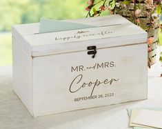 a white wooden box with the words mr and mrs written on it sitting next to a potted plant