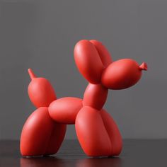 a red balloon dog sitting on top of a wooden table next to a gray wall