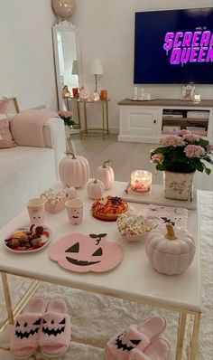 a white table topped with lots of food and drinks next to a tv screen in a living room