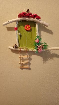 a small green door with flowers on the outside and a ladder leading up to it