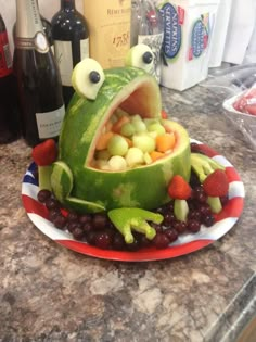 a watermelon shaped like a frog sitting on top of grapes and strawberries