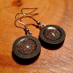 the earrings are black and brown with silver flecks on them, sitting on a wooden surface