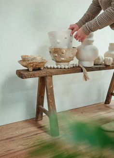 a person standing over a wooden table with bowls and vases on top of it