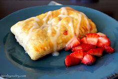 a pastry with icing and strawberries on a blue plate next to some sliced strawberries