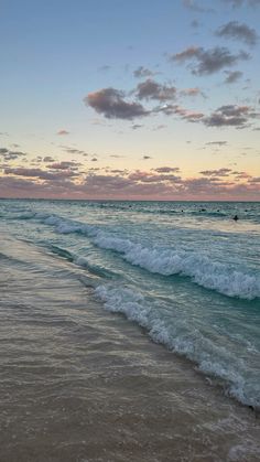 the ocean waves are rolling in to shore at sunset time, with people swimming in the water