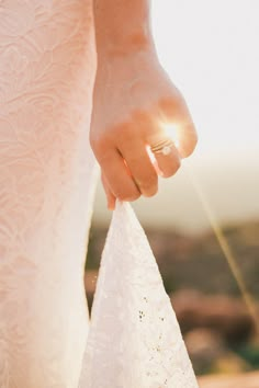 a close up of a person's hand holding a wedding dress in the sunlight