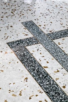 a black and white cross on the ground in front of a tiled floor with gold confetti