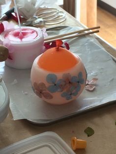 an orange and white vase sitting on top of a table next to plastic containers filled with paint