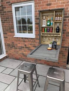 two metal stools sitting next to a table with bottles on it and an open storage unit in the back