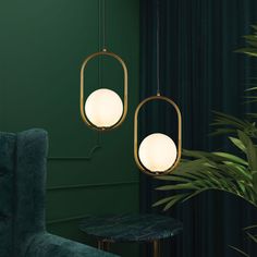 two lights hanging from a green wall next to a chair and table with a plant in the corner