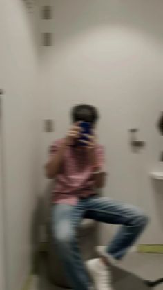 a man sitting on top of a toilet next to a white sink in a bathroom