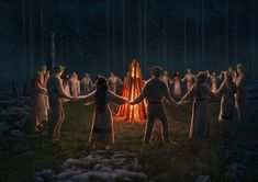 a group of people standing around a fire in the woods at night with their arms wrapped around each other