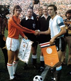 two soccer players shaking hands at the end of a game, with an audience in the background