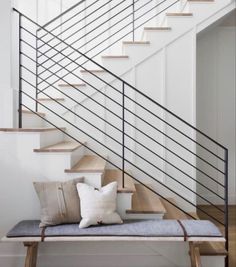 a white staircase with wooden steps and pillows on the bench in front of it,