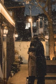 two people standing outside in the snow with their arms wrapped around each other, hugging