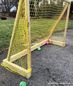 a yellow soccer goal with balls in it on the ground next to some grass and trees