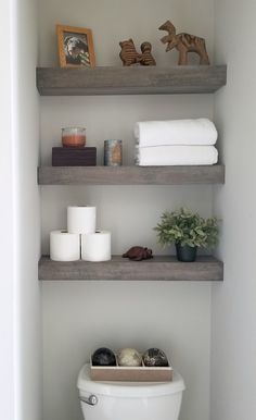 a toilet sitting in a bathroom next to two shelves filled with towels and other items