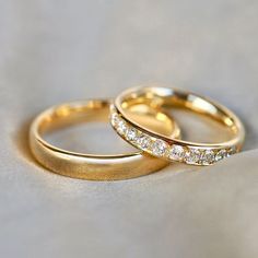 two gold wedding rings sitting on top of a white surface with one diamond set in the middle