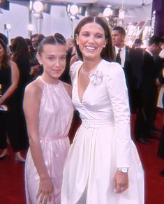 two women standing next to each other on a red carpet with people in the background