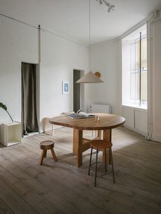 a table and chairs in a room with wood flooring, white walls and large windows