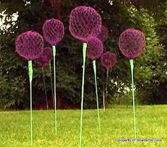 five purple flowers are in the grass near some trees and bushes, with green sticks sticking out of them