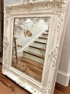 a white framed mirror sitting on top of a wooden floor next to a stair case