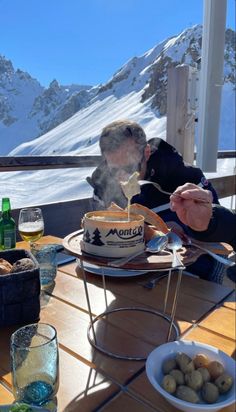 a man is blowing out the candles on his cake while sitting at a table in front of mountains