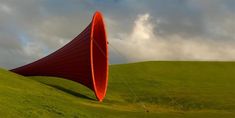 a large red cone sitting on top of a lush green field under a cloudy sky